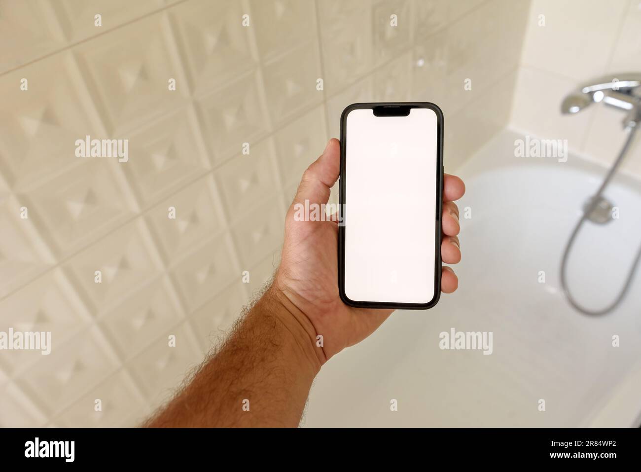 Smartphone mockup in bagno, uomo che tiene il telefono cellulare con schermo a sfioramento vuoto sopra la vasca da bagno, messa a fuoco selettiva Foto Stock