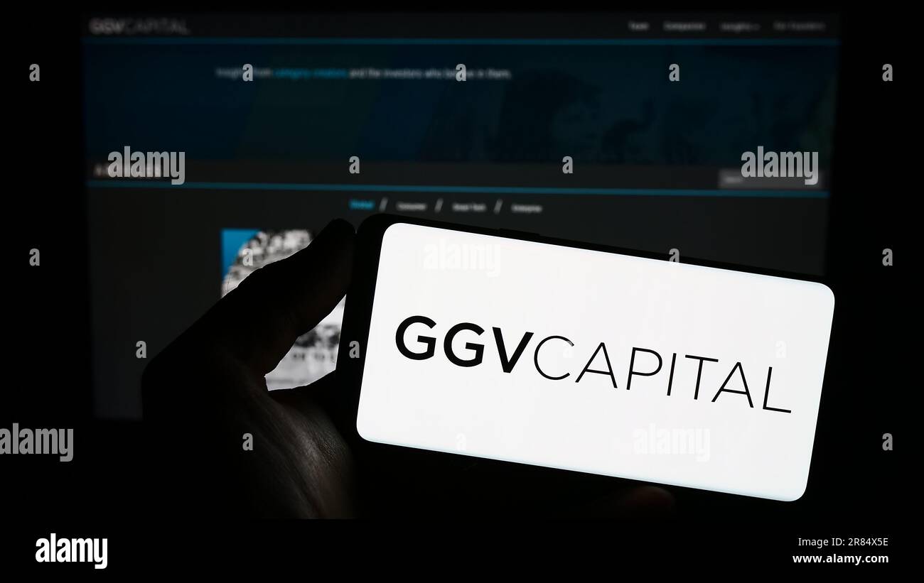Persona che tiene uno smartphone con il logo della società di investimento GGV Capital sullo schermo di fronte al sito Web. Messa a fuoco sul display del telefono. Foto Stock