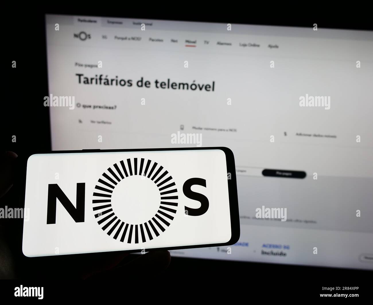Persona che detiene un telefono cellulare con il logo della società di telecomunicazioni NOS SGPS SA sullo schermo di fronte alla pagina Web aziendale. Messa a fuoco sul display del telefono. Foto Stock