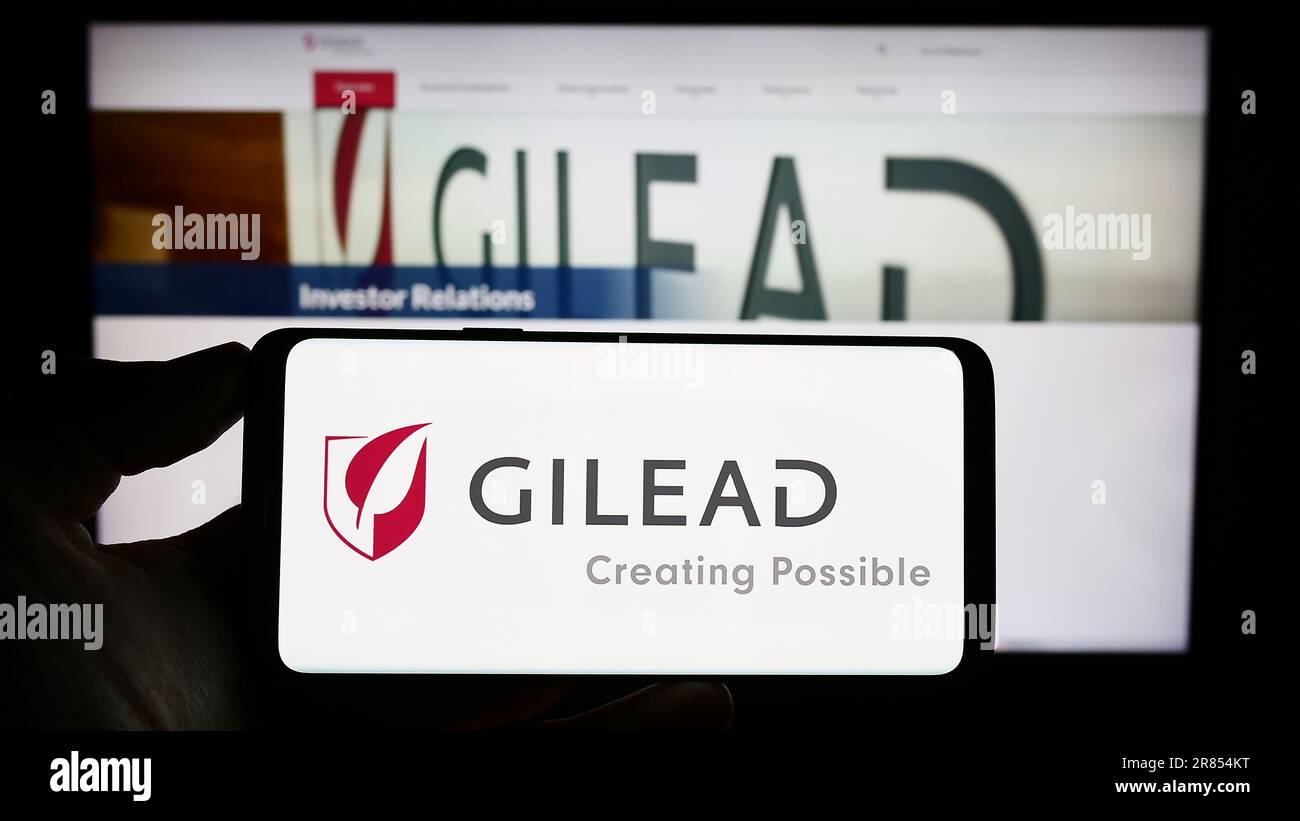 Persona che tiene uno smartphone con il logo della società biofarmaceutica americana Gilead Sciences Inc. Sullo schermo di fronte al sito Web. Messa a fuoco sul display del telefono. Foto Stock