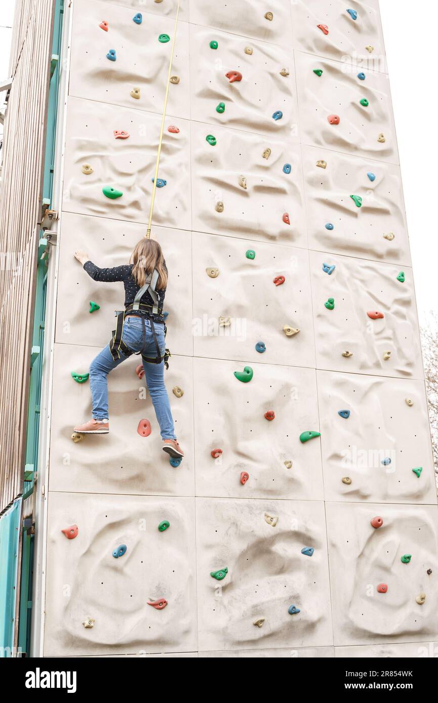 Adolescente ragazza afferrare parete artificiale di arrampicata con palle spaccate. Imbracatura per arrampicata attrezzatura sportiva di sicurezza. Rope parco di divertimenti della città, ostac Foto Stock