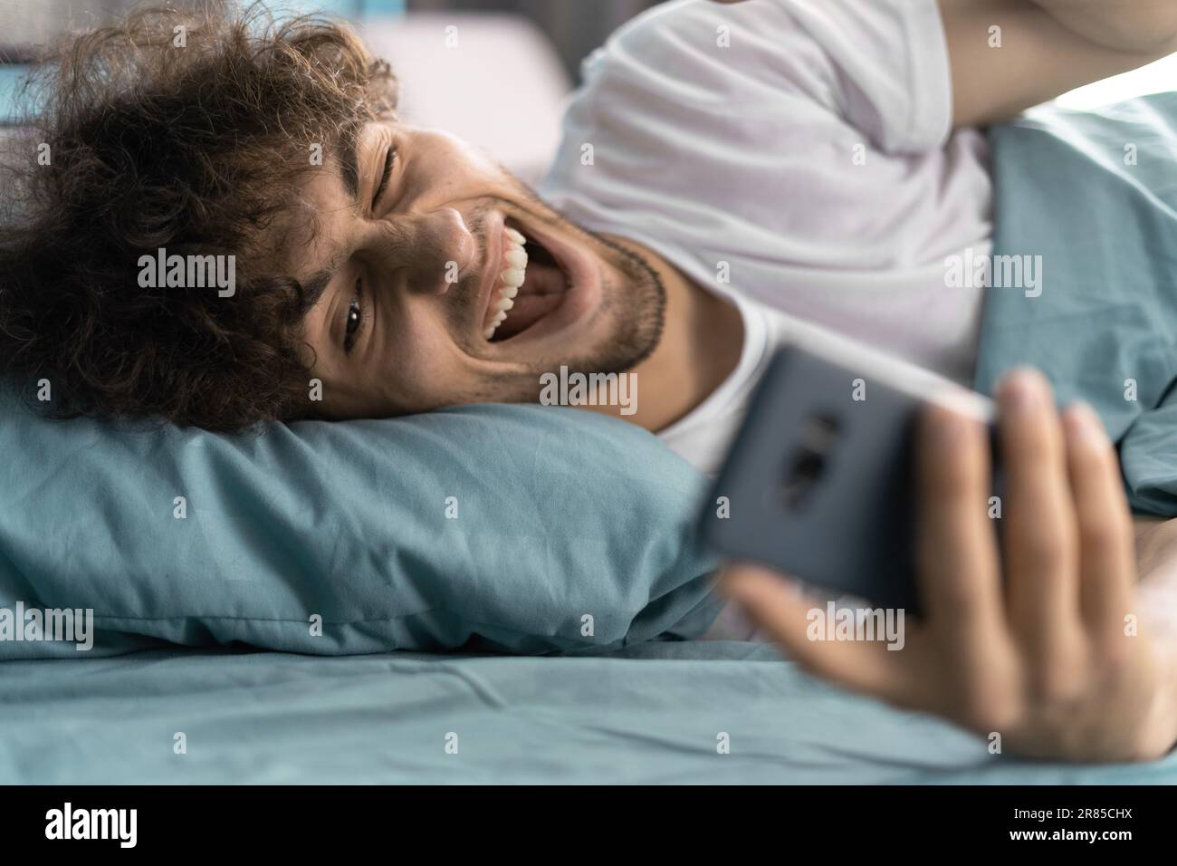 Buon uomo arabo videochiamare una ragazza su uno smartphone sul letto dopo il risveglio al mattino Foto Stock