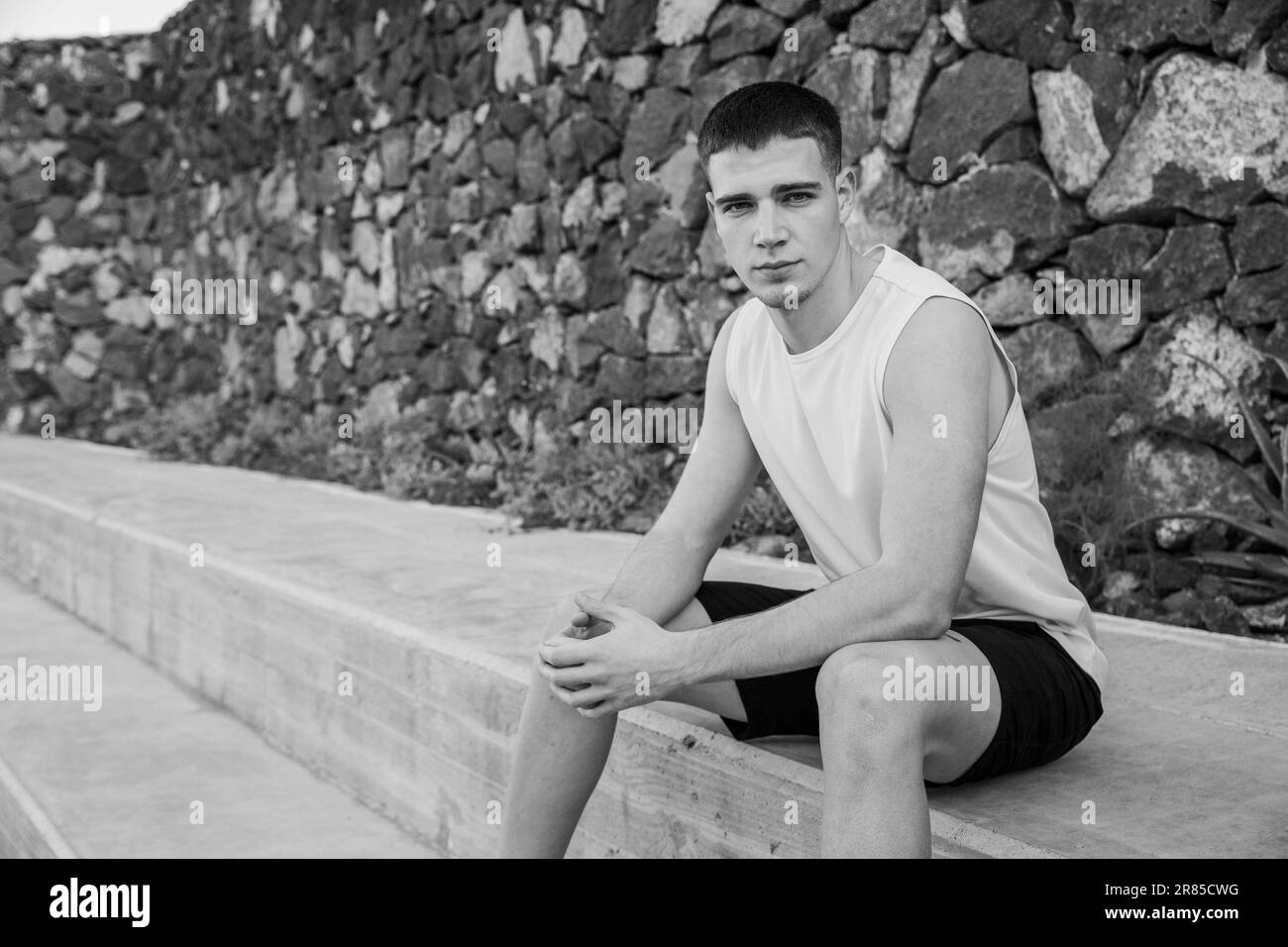 Un ragazzo adolescente è seduto al bordo di un campo di pallacanestro, foto in bianco e nero Foto Stock