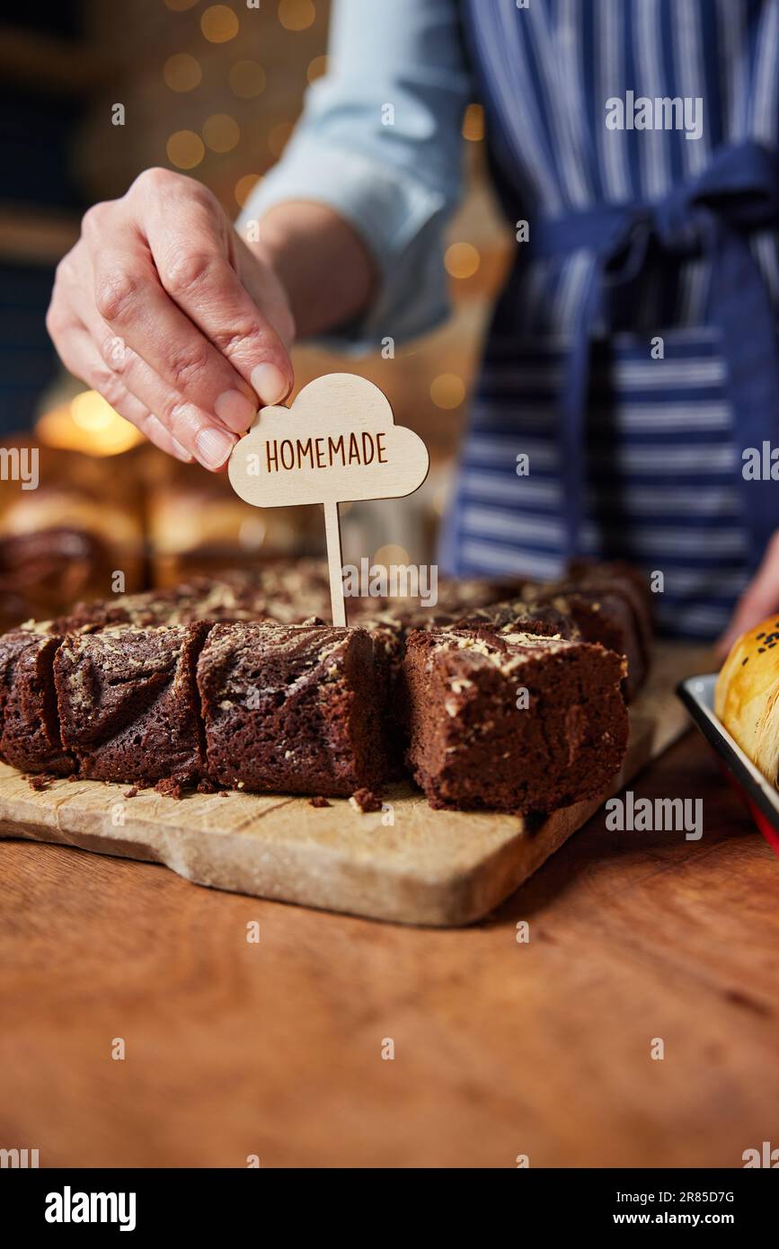 Sales Assistant in Bakery mettere l'etichetta fatta in casa in brownie al cioccolato appena sfornate Foto Stock