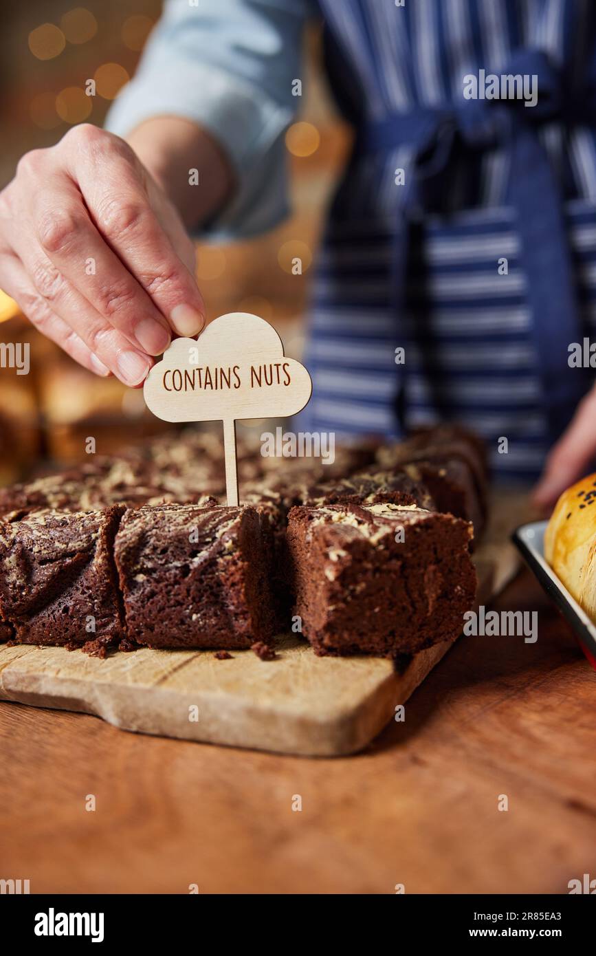 Sales Assistant in Bakery Putting contiene l'etichetta delle noci in brownie al cioccolato appena sfornate Foto Stock