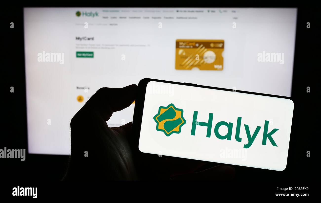 Persona che tiene il cellulare con il logo della società di servizi finanziari kazako Halyk Bank sullo schermo di fronte al sito web aziendale. Messa a fuoco sul display del telefono. Foto Stock