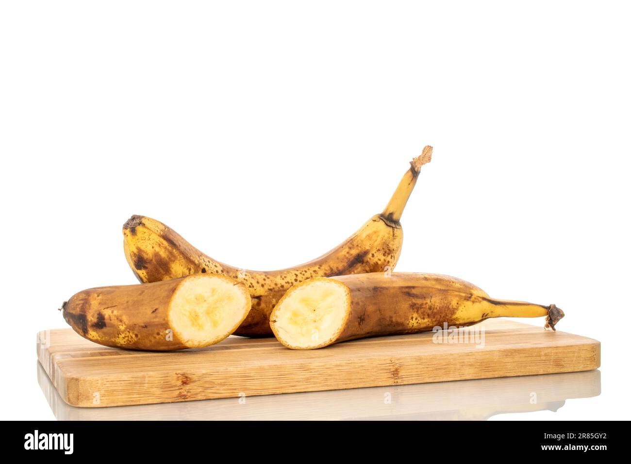 Una banana matura intera e una metà con un coltello su un tavolo da cucina in legno, macro, isolata su sfondo bianco. Foto Stock