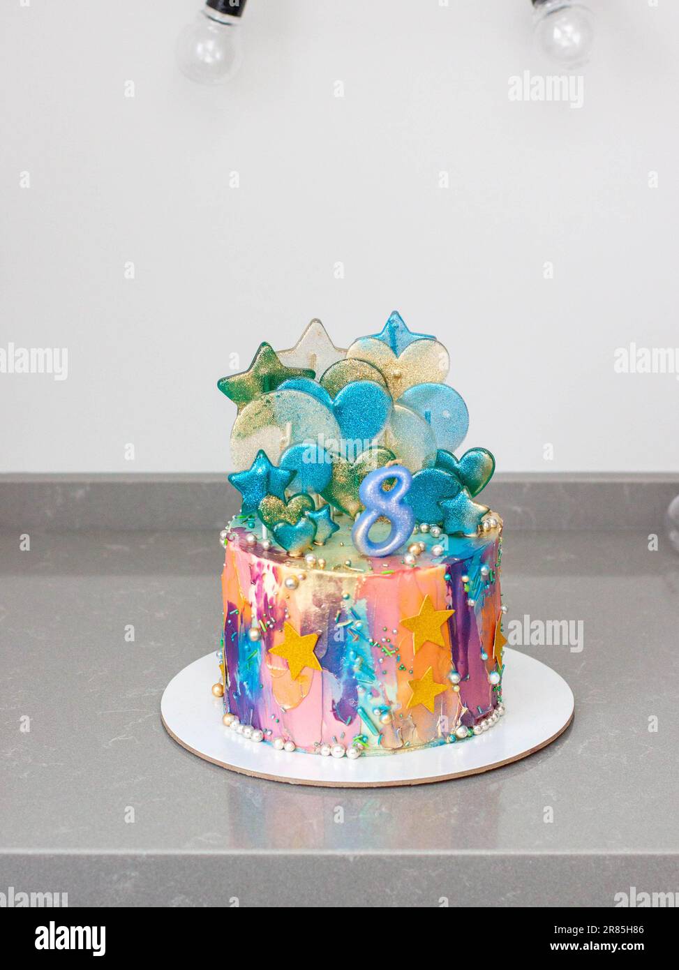 Vivace torta colorata glittery con numero 8, lecca, stelle commestibili, spruzzi su sfondo festivo Foto Stock