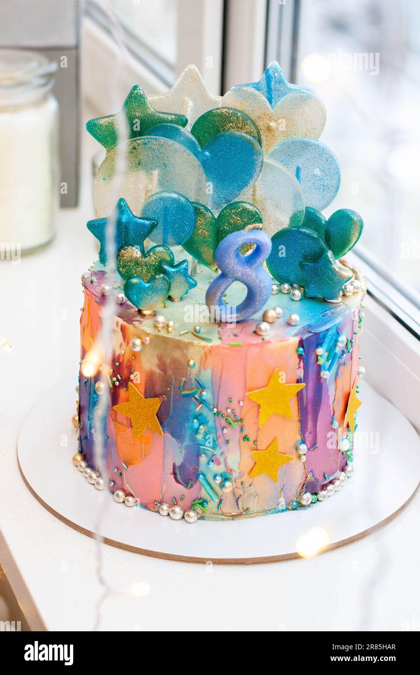 Vivace torta colorata glittery con numero 8, lecca, stelle commestibili, spruzzi su sfondo festivo Foto Stock