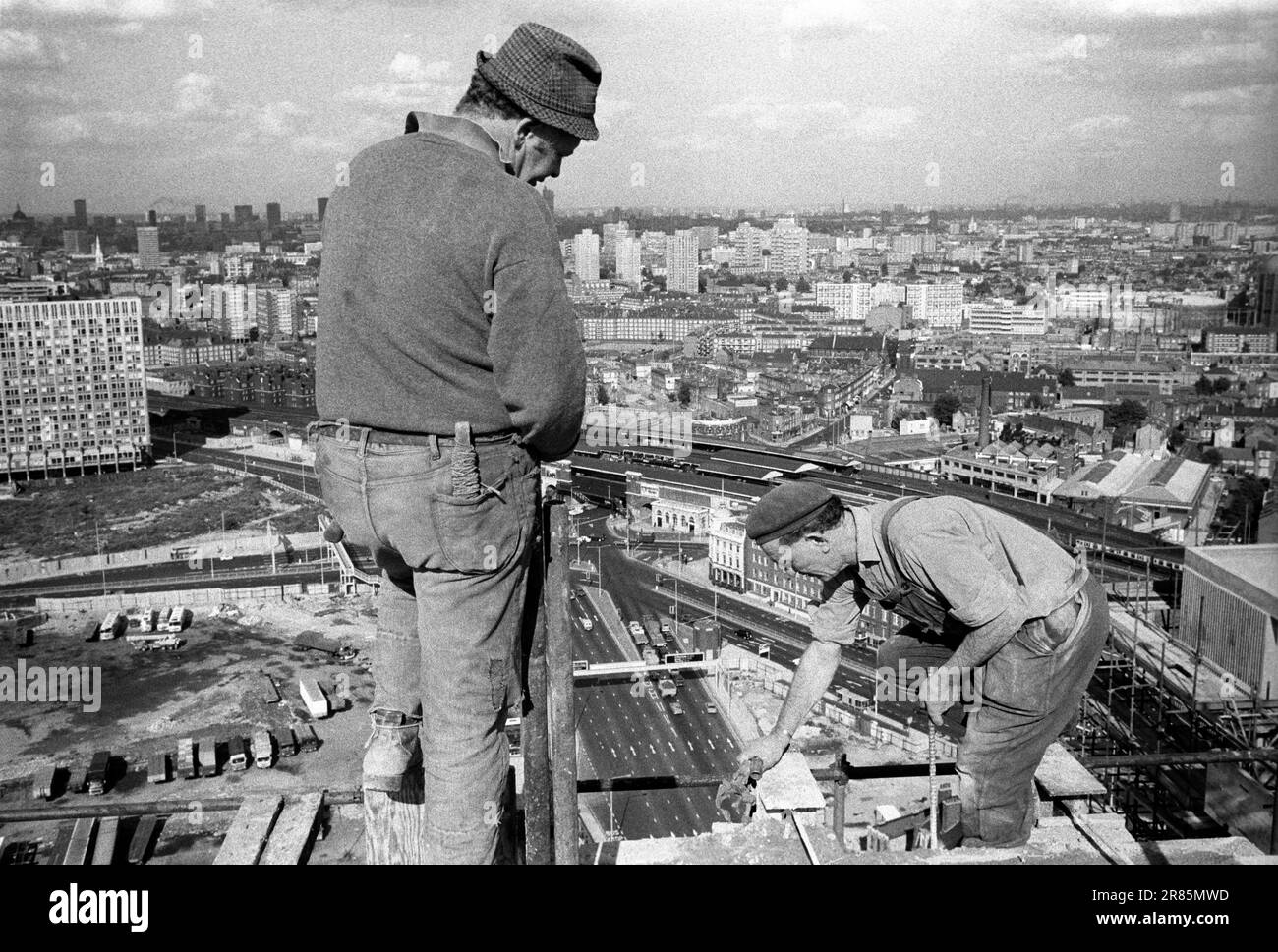 Vista del paesaggio urbano di Londra degli anni '1970 Un navvie navvy irlandese, un operaio edile in cima e che lavora su un blocco torre Nine Elms. Vauxhall Cross sotto di loro e lo skyline del sud di Londra. Londra, Inghilterra 1974 Regno Unito. HOMER SYKES Foto Stock