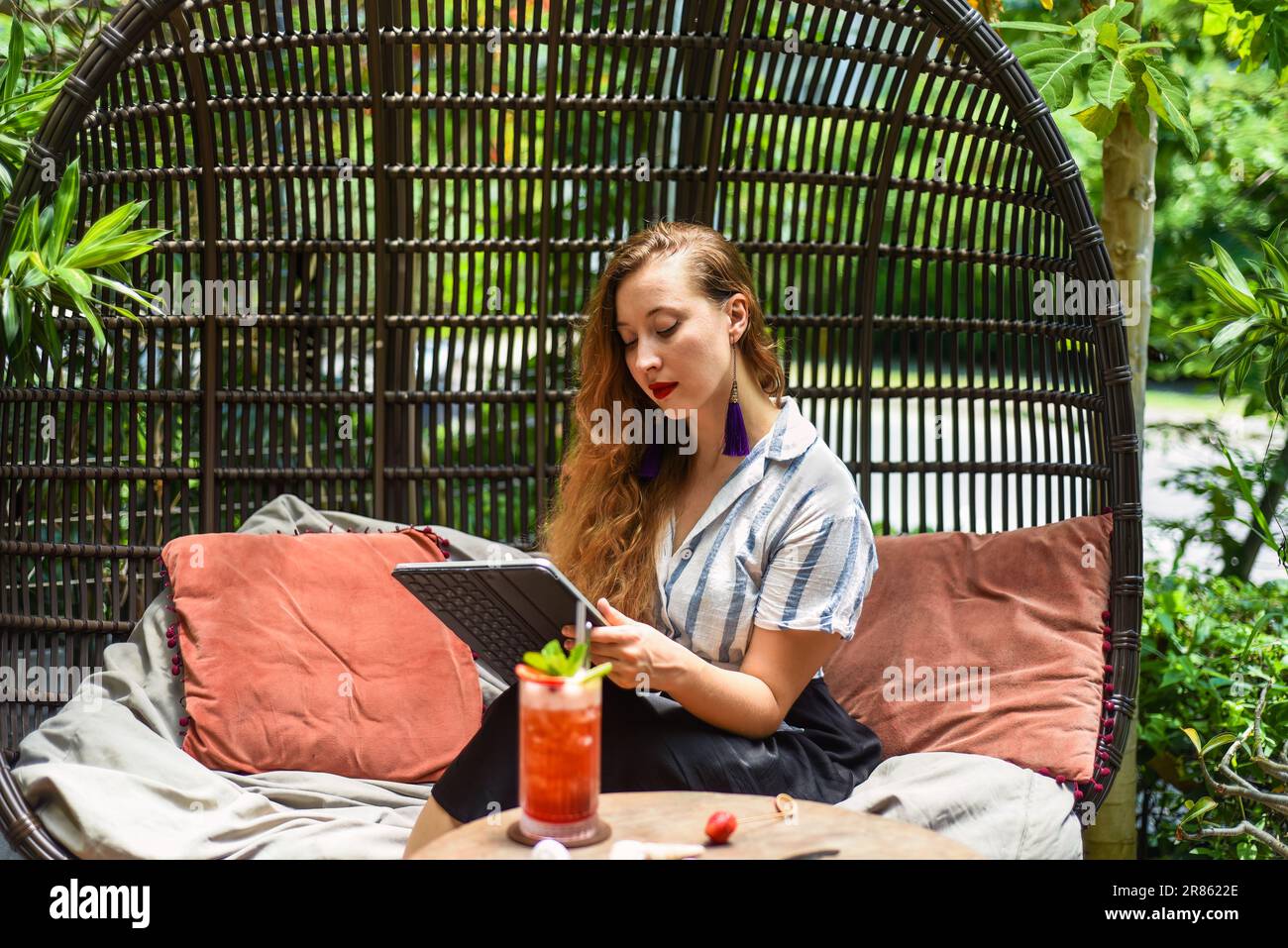 Bella artista e illustratrice bionda che pensa a un concetto del suo disegno, seduta accanto al tavolo con un tablet elettronico e uno stilo Foto Stock