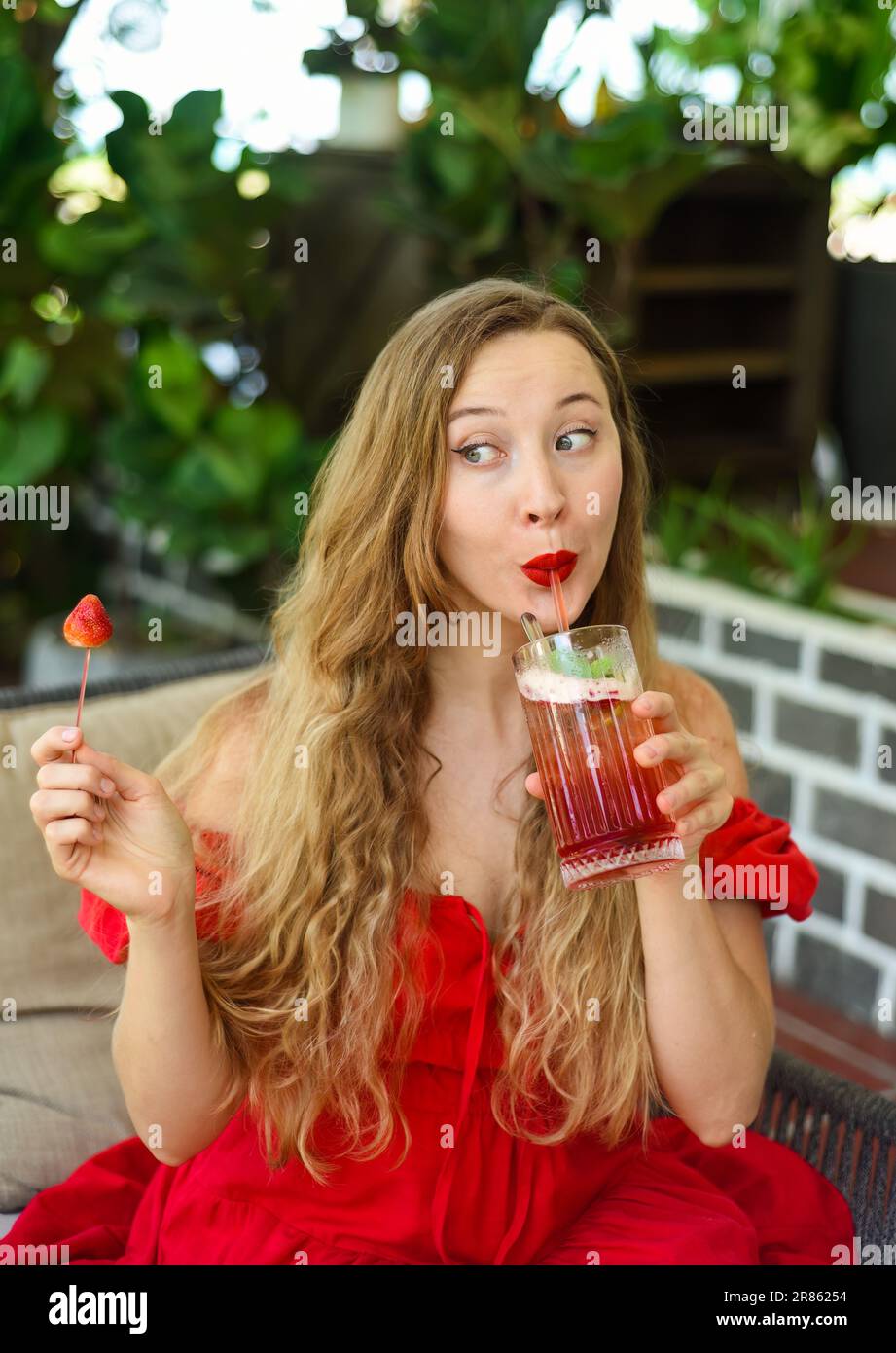 Bella donna bionda russa che beve tè alle fragole e guarda le fragole Foto Stock