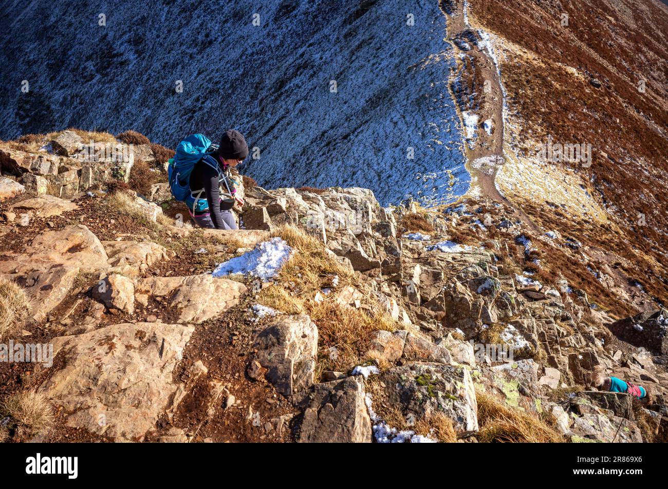 Una ragazza escursionista che scende un ripido sentiero roccioso verso Sail da Crag Hill con il proprio cane in inverno nel Lake District inglese, Regno Unito. Foto Stock