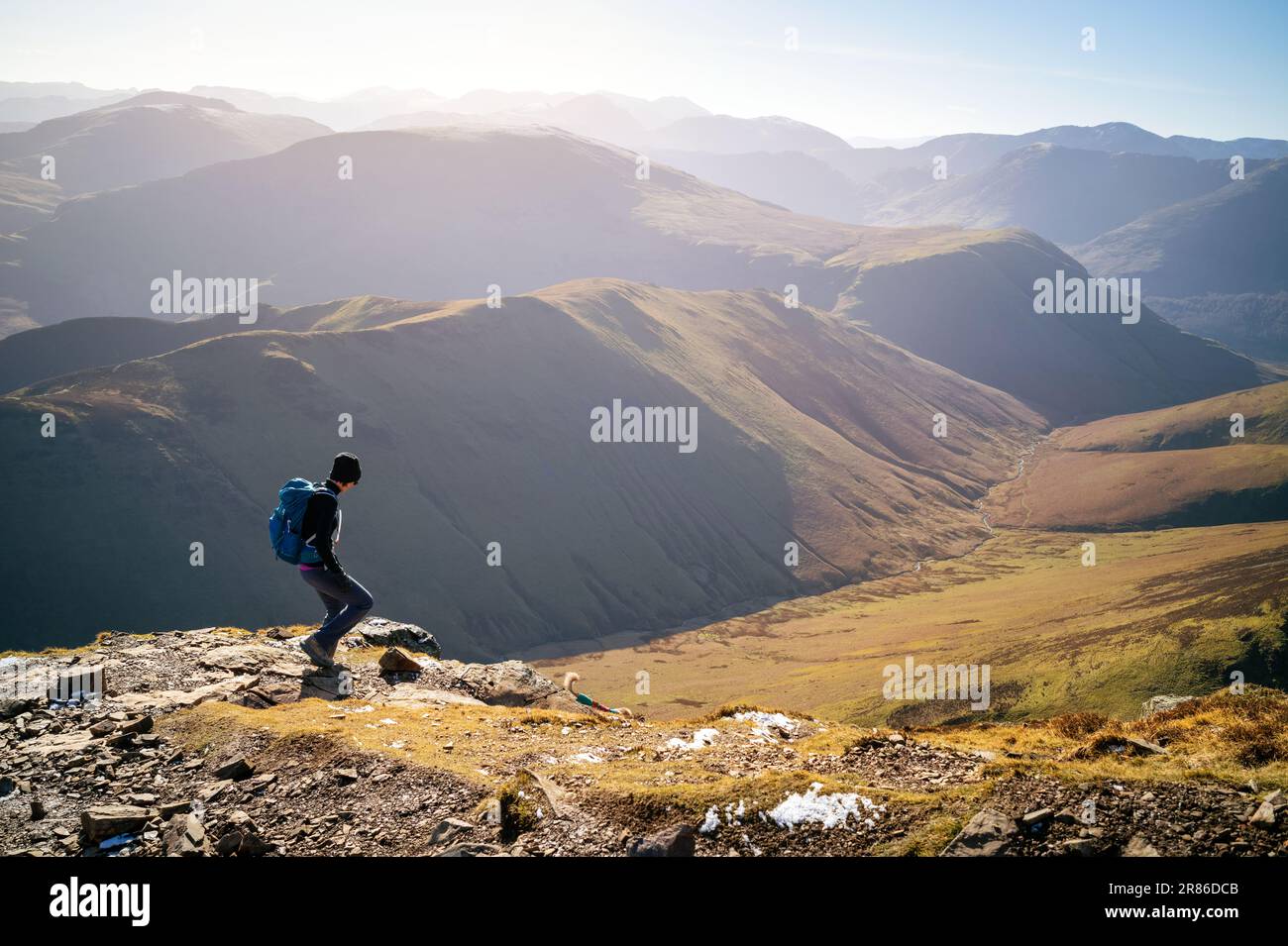 Un escursionista femminile che scende un sentiero roccioso verso Sail da Crag Hill con le cime di High Snockrigg e Robinson in inverno nel Distretto Inglese del Lago Foto Stock