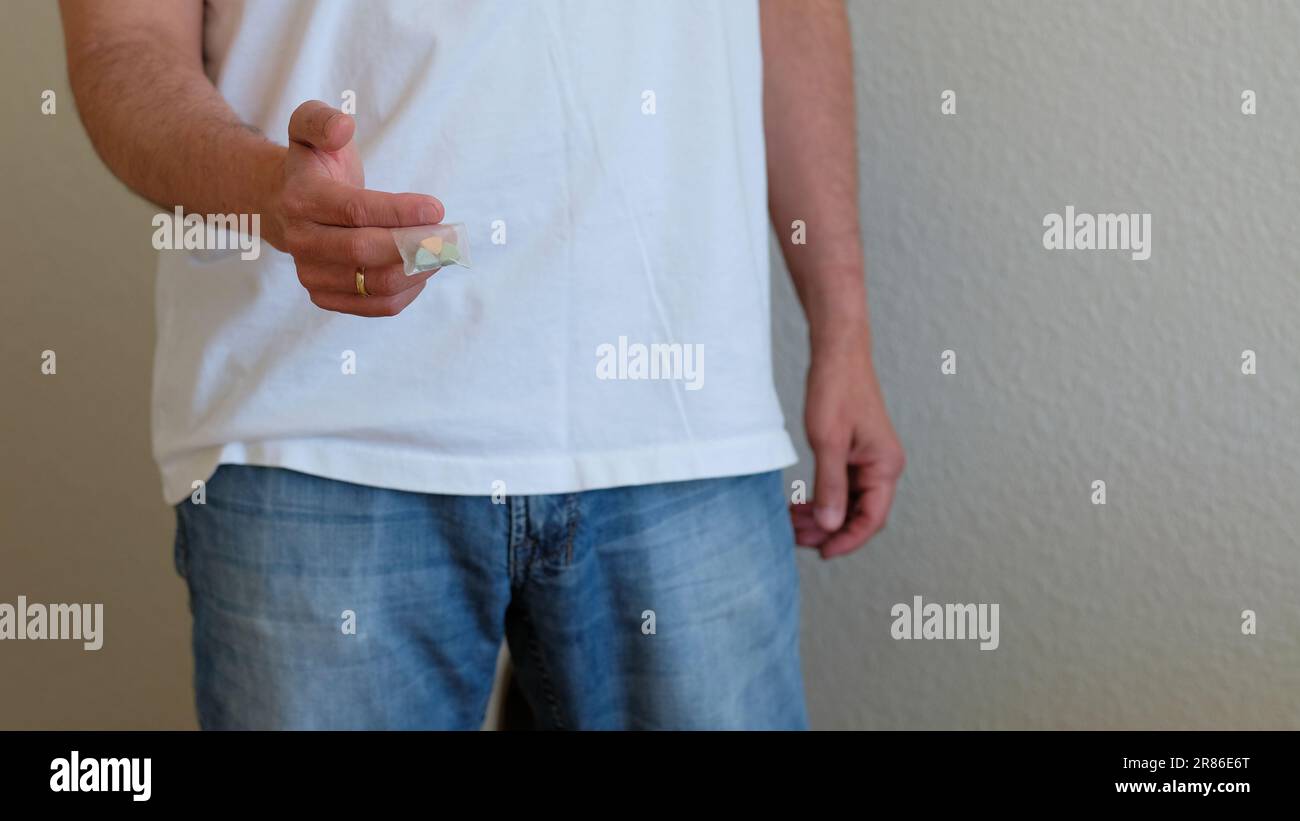 Uomo che offre pillole di ecstasy Tesla in un sacchetto di plastica; a forma di scudo con il logo Tesla; 240 milligrammi di MDMA Molly ricreativa, farmaci. Foto Stock
