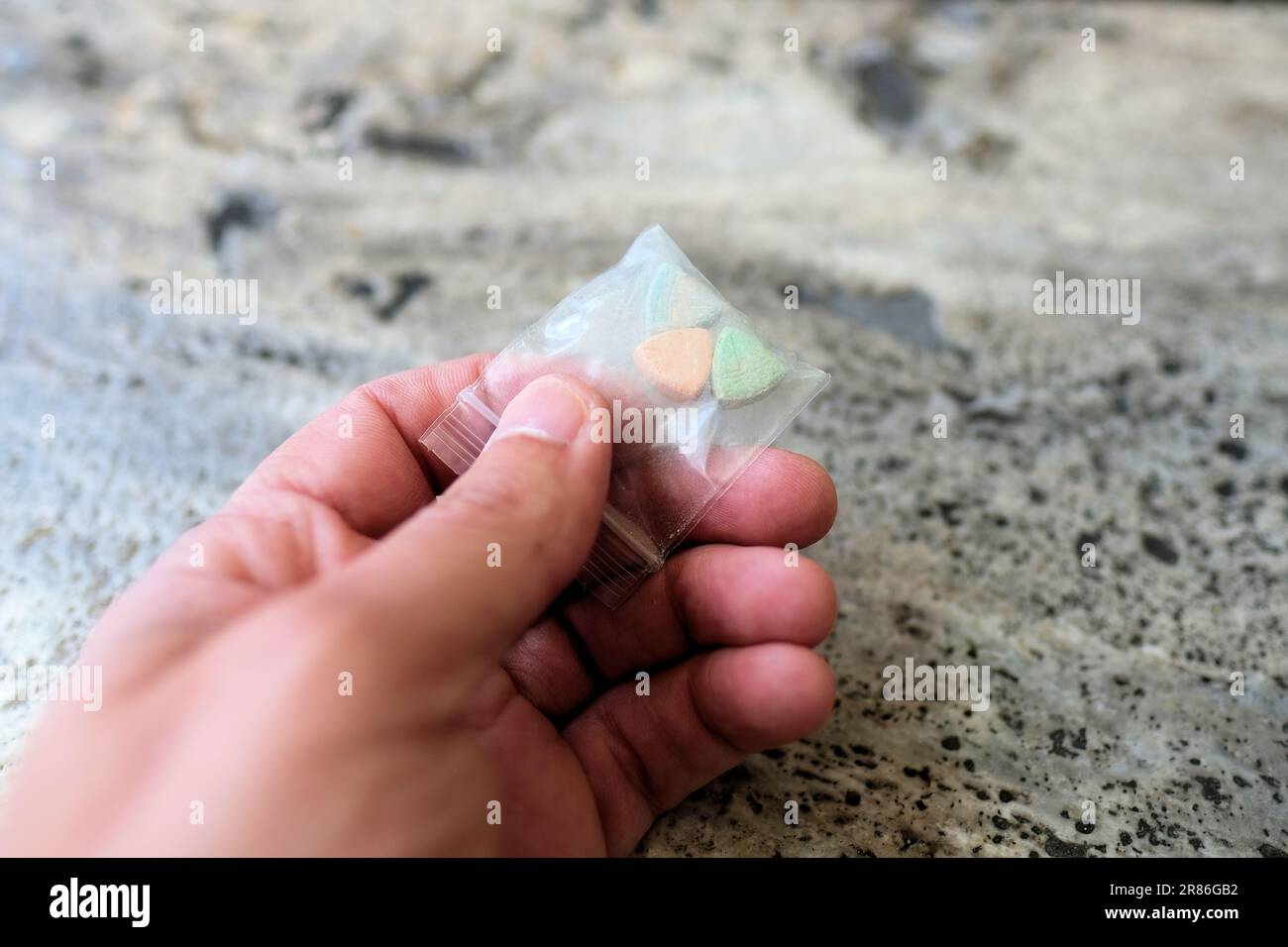 Mano che tiene le pillole di ecstasy Tesla di colore arancione, verde e blu a forma di scudo con il logo Tesla; 240 milligrammi di MDMA ricreativo. Foto Stock