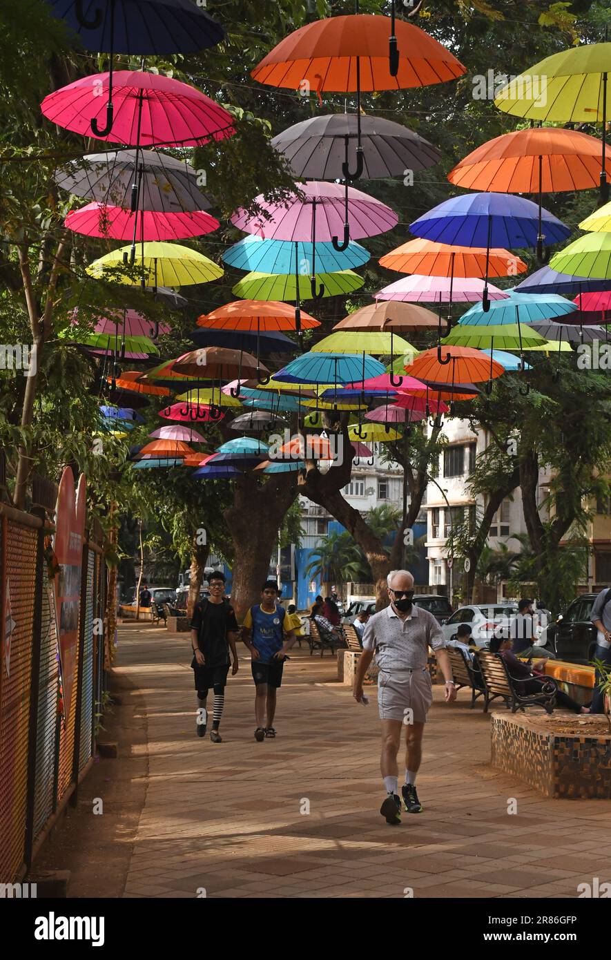 Mumbai, India. 19th giugno, 2023. Si vedono persone che camminano sotto colorati ombrelli installati in un vicolo fuori da un parco giochi a Mumbai. Gli ombrelli sono impiccati come parte del piano di abbellimento prima della stagione monsonica. Credit: SOPA Images Limited/Alamy Live News Foto Stock