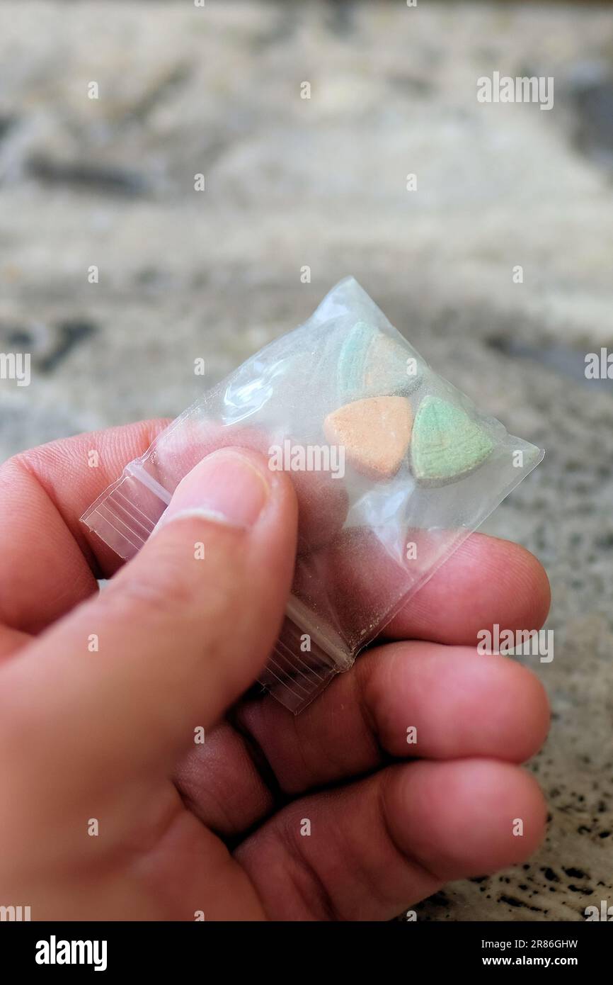 Mano che tiene le pillole di ecstasy Tesla di colore arancione, verde e blu a forma di scudo con il logo Tesla; 240 milligrammi di MDMA ricreativo. Foto Stock
