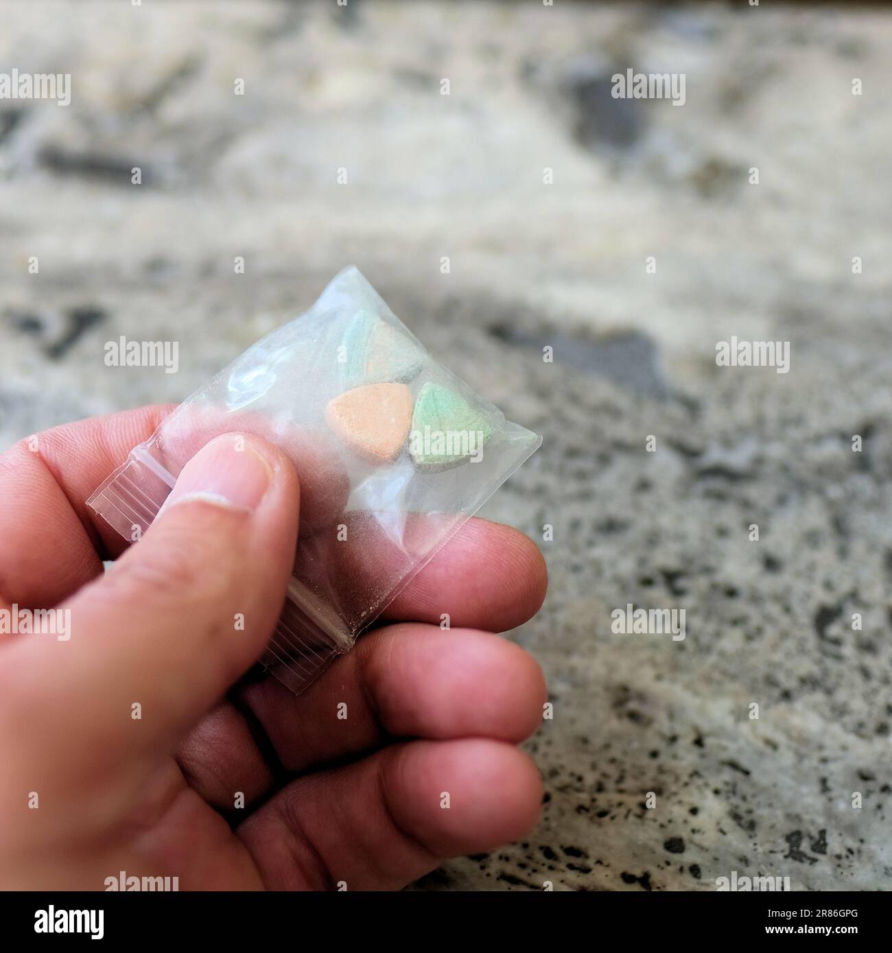 Mano che tiene le pillole di ecstasy Tesla di colore arancione, verde e blu a forma di scudo con il logo Tesla; 240 milligrammi di MDMA ricreativo. Foto Stock