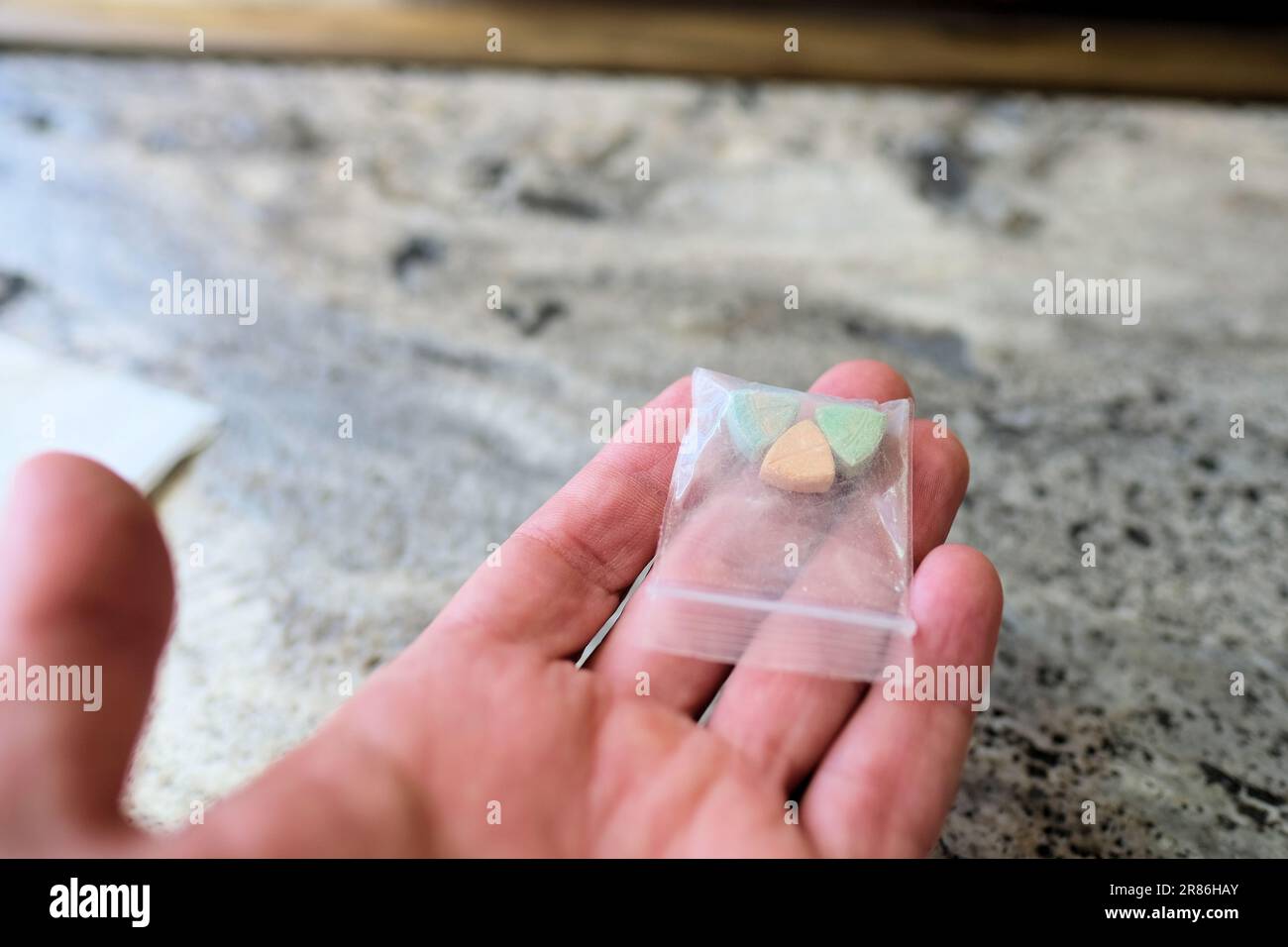 Mano che tiene le pillole di ecstasy Tesla di colore arancione, verde e blu a forma di scudo con il logo Tesla; 240 milligrammi di MDMA ricreativo. Foto Stock
