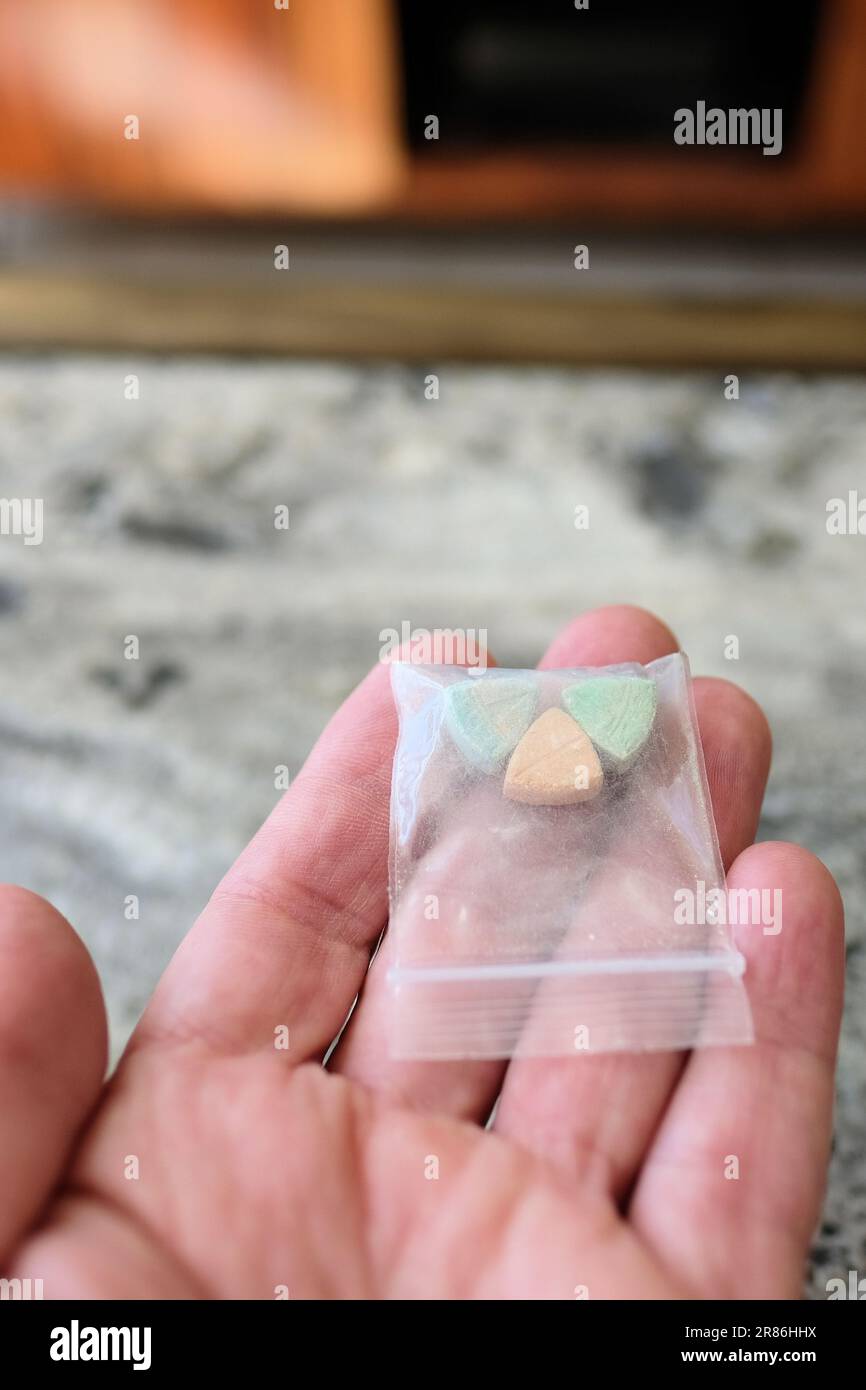 Mano che tiene le pillole di ecstasy Tesla di colore arancione, verde e blu a forma di scudo con il logo Tesla; 240 milligrammi di MDMA ricreativo. Foto Stock