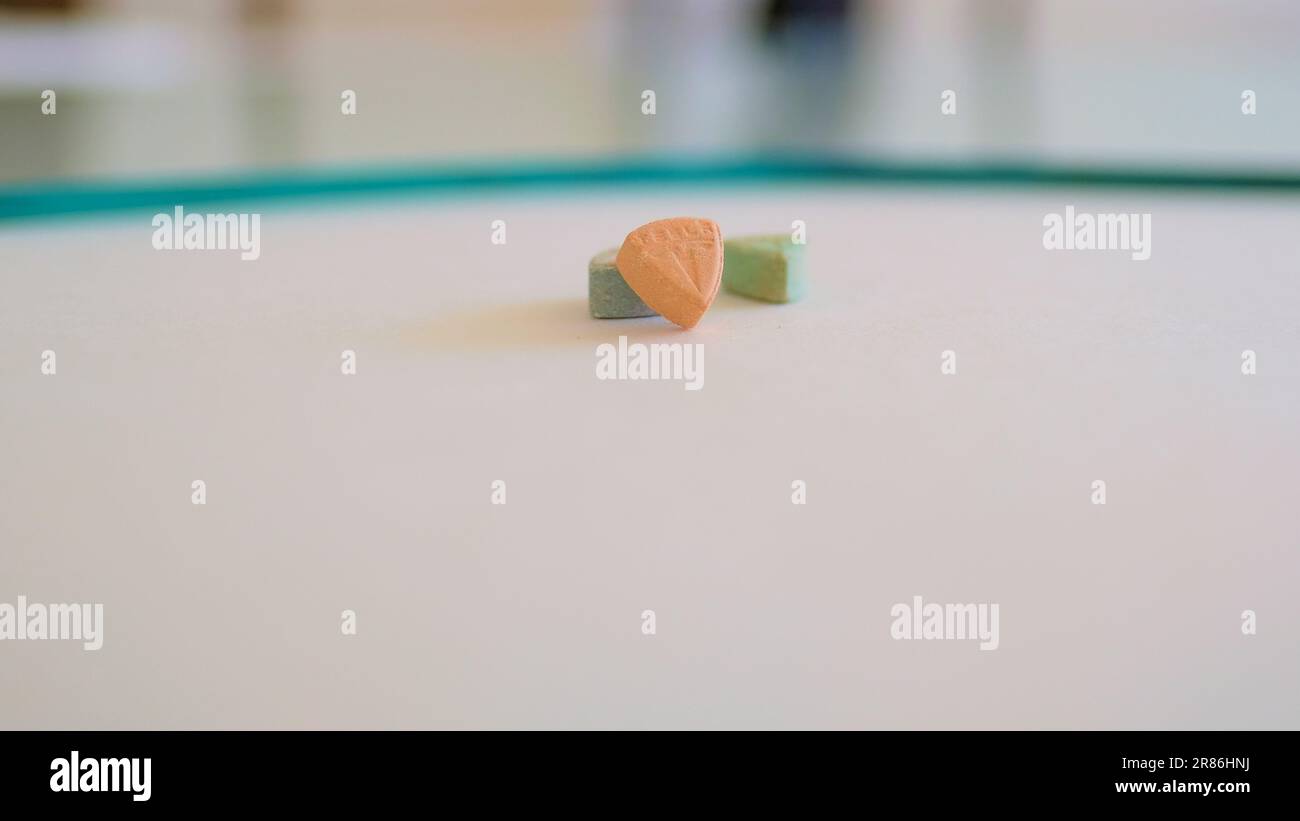 Pillole di ecstasy Tesla di colore arancione, verde e blu a forma di scudo con il logo Tesla; 240 milligrammi di farmaci ricreativi MDMA o Molly Foto Stock