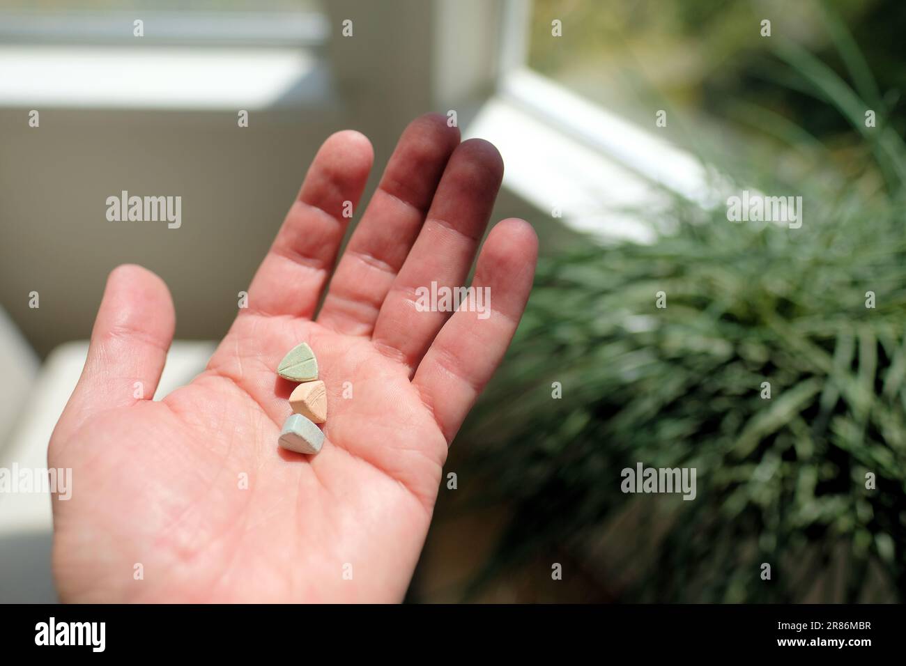 Mano che tiene le pillole di ecstasy Tesla di colore arancione, verde e blu a forma di scudo con il logo Tesla; 240 milligrammi di MDMA ricreativo. Foto Stock