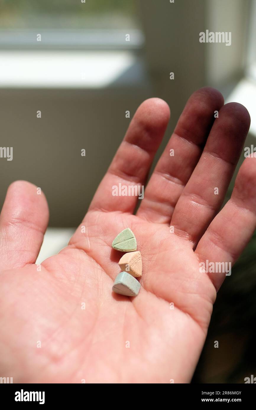 Mano che tiene le pillole di ecstasy Tesla di colore arancione, verde e blu a forma di scudo con il logo Tesla; 240 milligrammi di MDMA ricreativo. Foto Stock