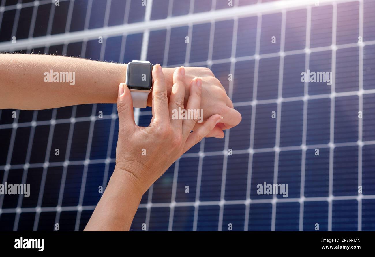 Smartwatch su mano femmina sullo sfondo del pannello a energia solare. controllo remoto della stazione di energia solare domestica. Foto Stock