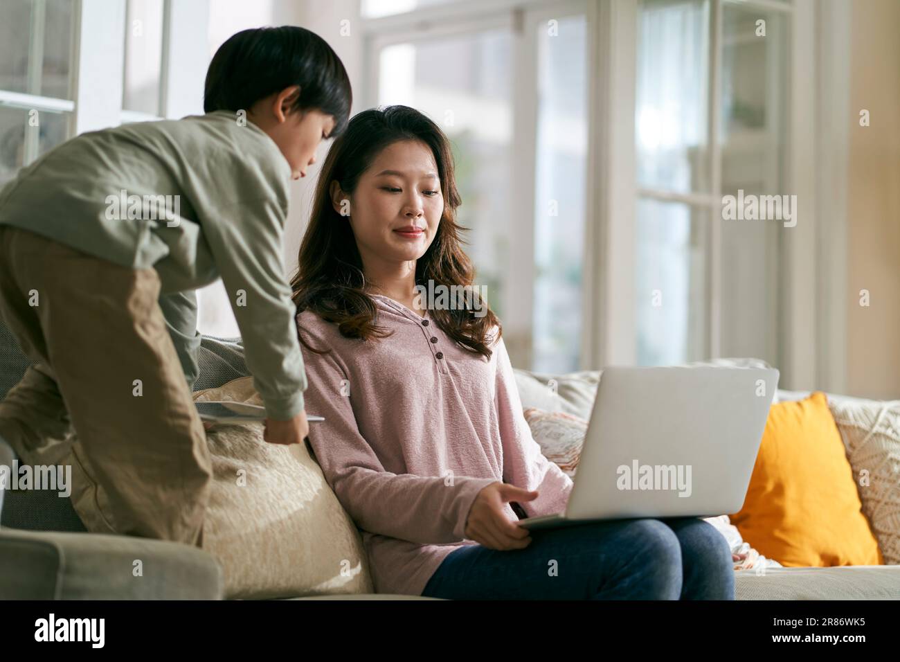 giovane madre asiatica d'affari cercando di lavorare a casa infastidita da figlio iperattivo Foto Stock