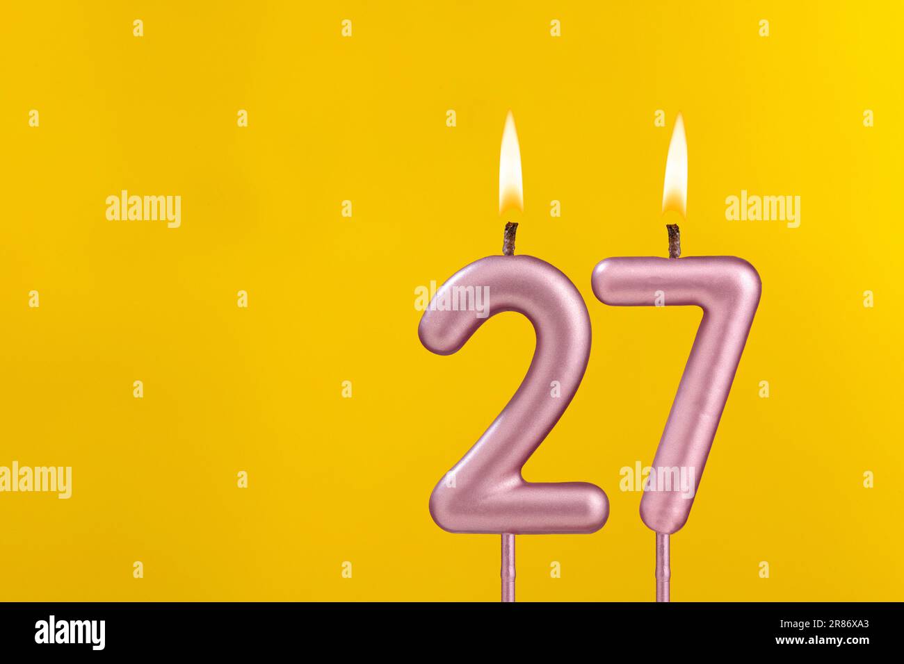 Candela di compleanno numero 27 - celebrazione di compleanno su sfondo giallo Foto Stock