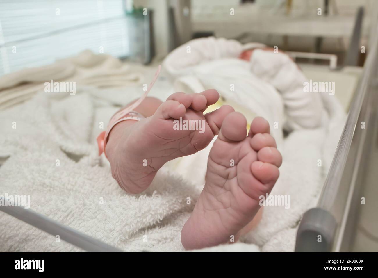 Primo piano di un piccolo paio di piedi e dita dei piedi del neonato avvolto in una coperta con un braccialetto in plastica etichetta identità nella sala parto in hospit Foto Stock