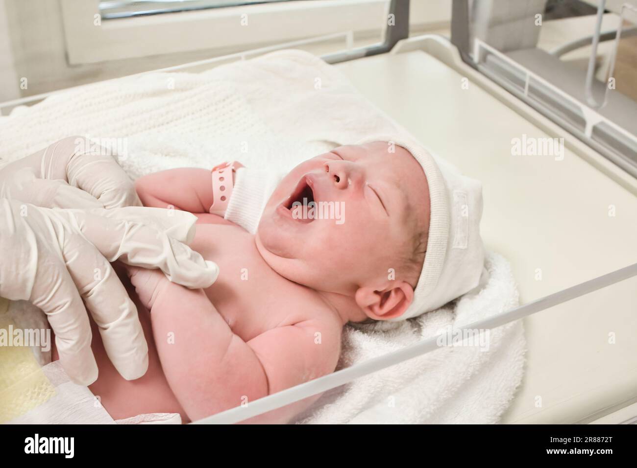 Un neonato che indossa un braccialetto d'identità in plastica che viene collocato in una culla da un'infermiera nella sala parto in un reparto di maternità in ospedale - concetto di Foto Stock