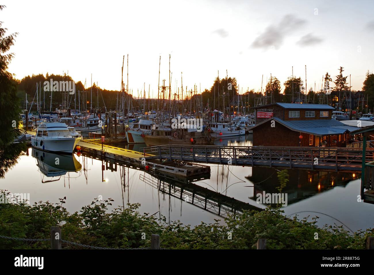 Atmosfera serale in un piccolo porto, illuminato houseboat e jetties, Ucluelet, Pacifico, Vancouver isalnd, British Columbia, Canada Foto Stock