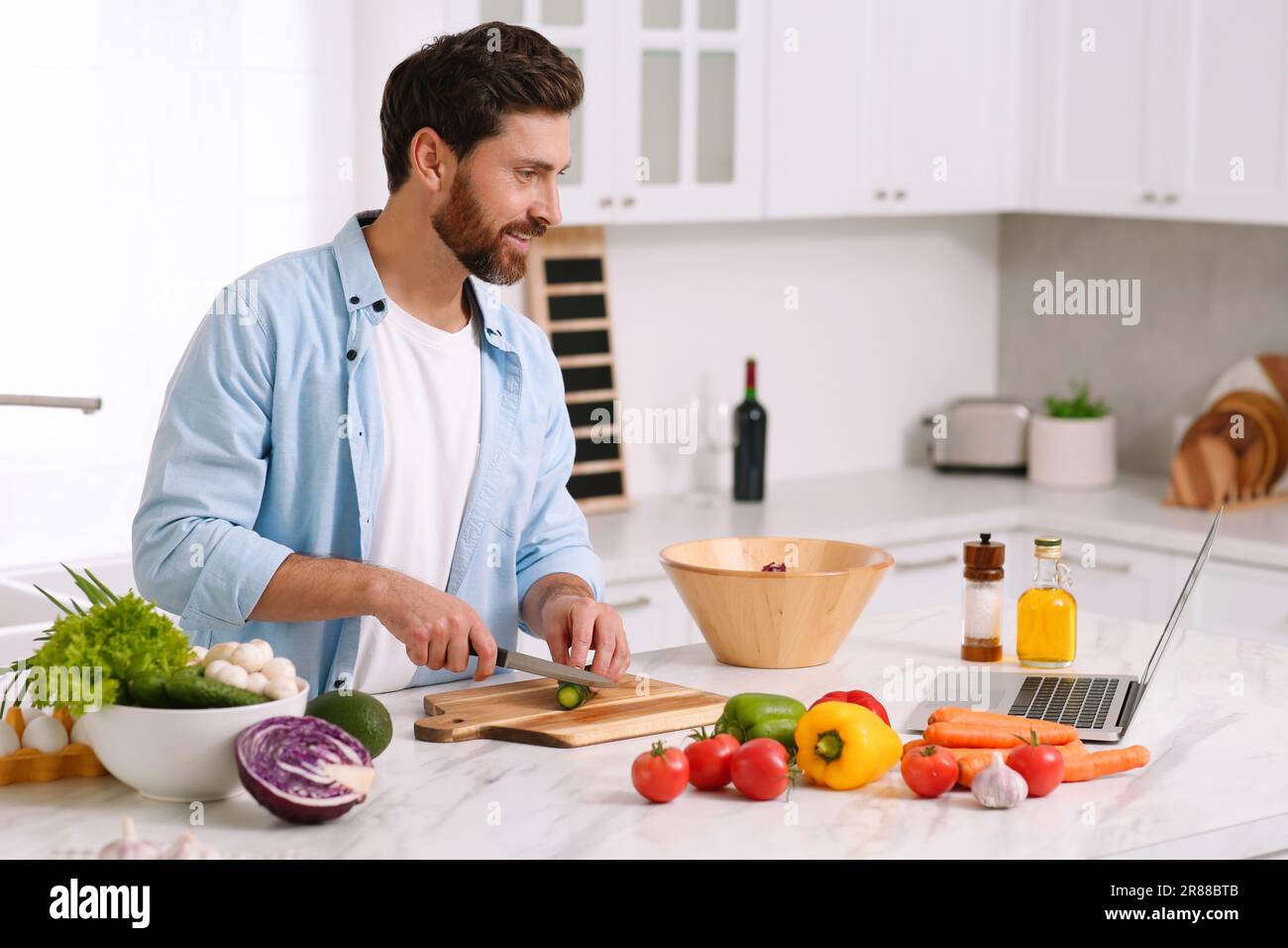 Uomo che fa la cena mentre guarda corso di cucina on-line tramite computer portatile in cucina Foto Stock