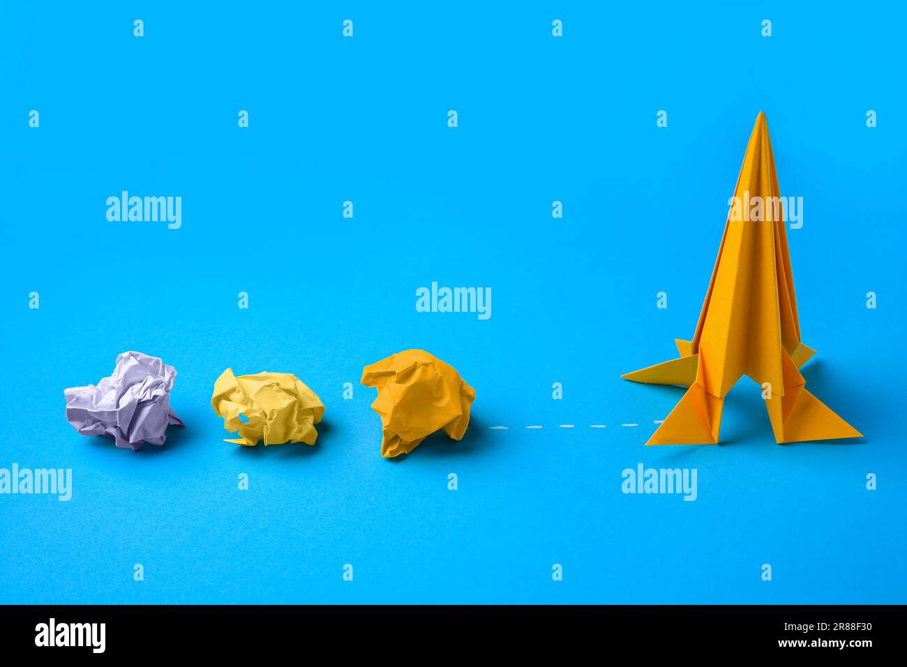 Razzo arancione fatto a mano e pezzi di carta sgualciti su sfondo azzurro Foto Stock