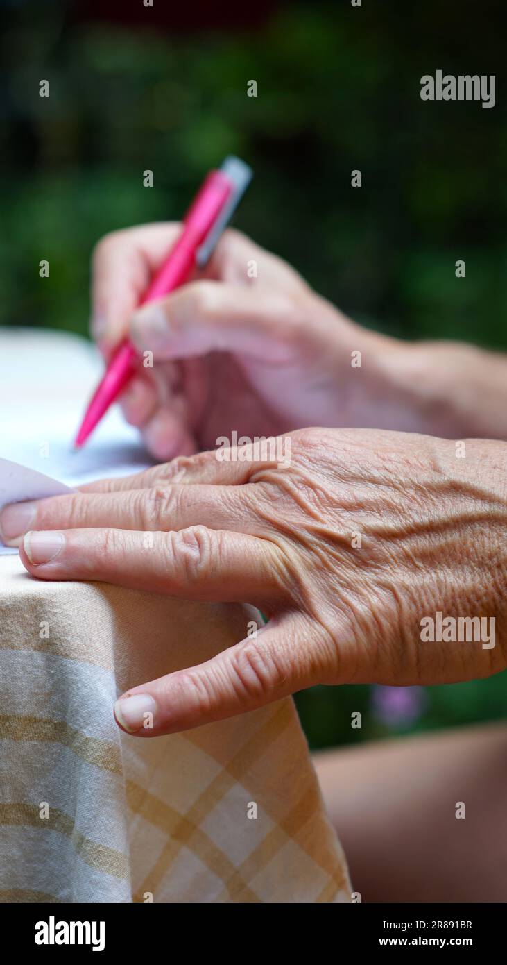 Le mani di un uomo che scrive con una penna rosa. Foto Stock