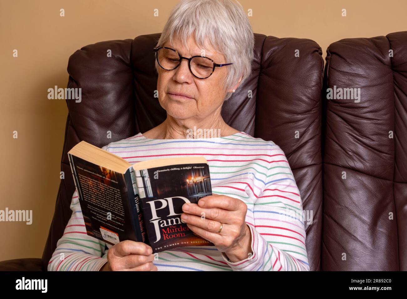 Donna che si rilassa a casa leggendo un romanzo di PD James Foto Stock