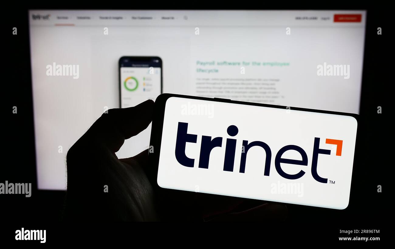 Persona che possiede il cellulare con il logo della società di outsourcing statunitense TriNet Group Inc. Sullo schermo davanti alla pagina Web aziendale. Concentrarsi sul display del telefono. Foto Stock
