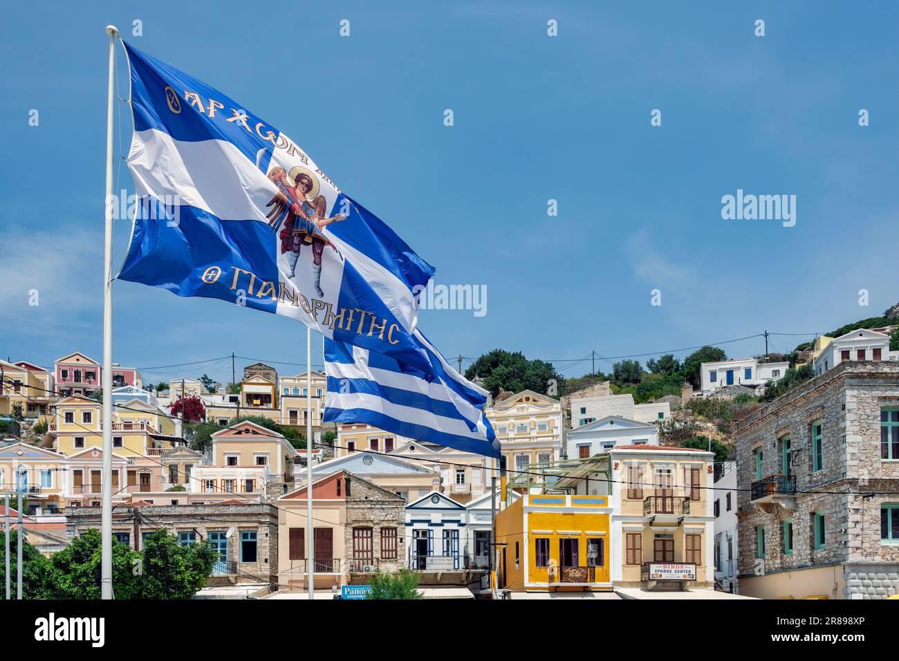 Griechische Flaggen auf der Brücke Kaldirimi auf Symi mit den Kapitänshäusern Foto Stock