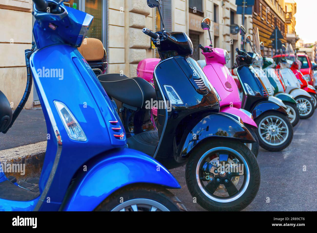Una serie di scooter Vespa multicolore parcheggiati in fila lungo la strada, noleggio scooter in città. Foto Stock