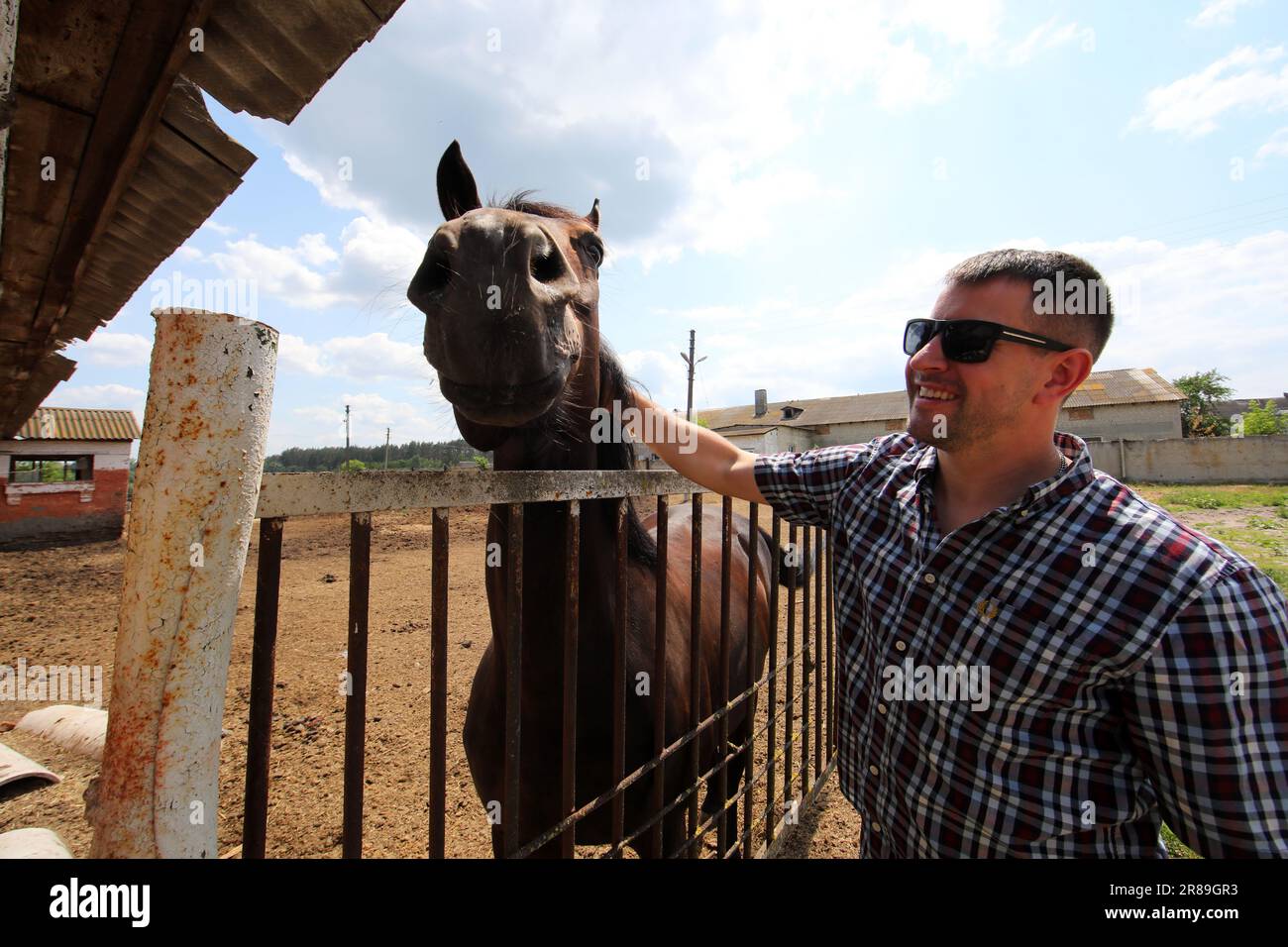 REGIONE DI KHARKIV, UCRAINA - 17 GIUGNO 2023 - Un uomo animali da compagnia un cavallo al Kharkiv Military Rehabilitation Centre che offre personale militare psychologica Foto Stock