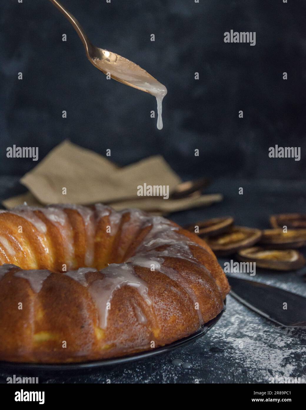 Torta all'arancia, cucchiaio con gocce di glassa su sfondo scuro. Fette di arancia disidratate. Sfondo rustico. Torta di ciambelle Foto Stock