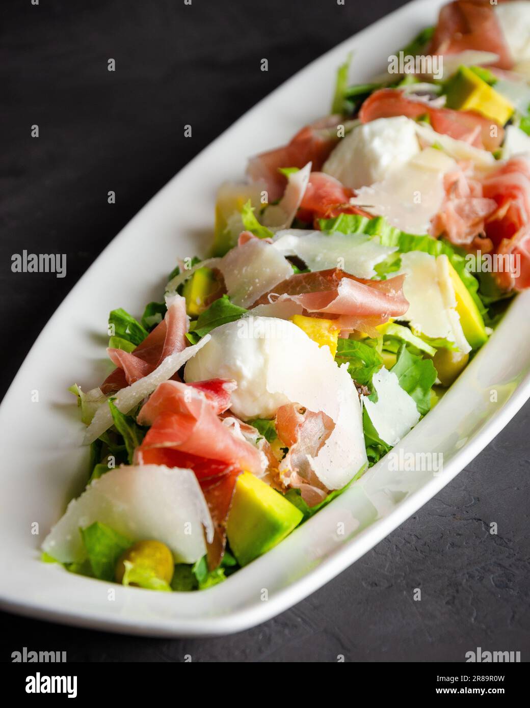 Insalata di formaggio di bufala e prosciutto serrano, accompagnata da avocado. Sfondo nero. Piatto bianco. Foto Stock