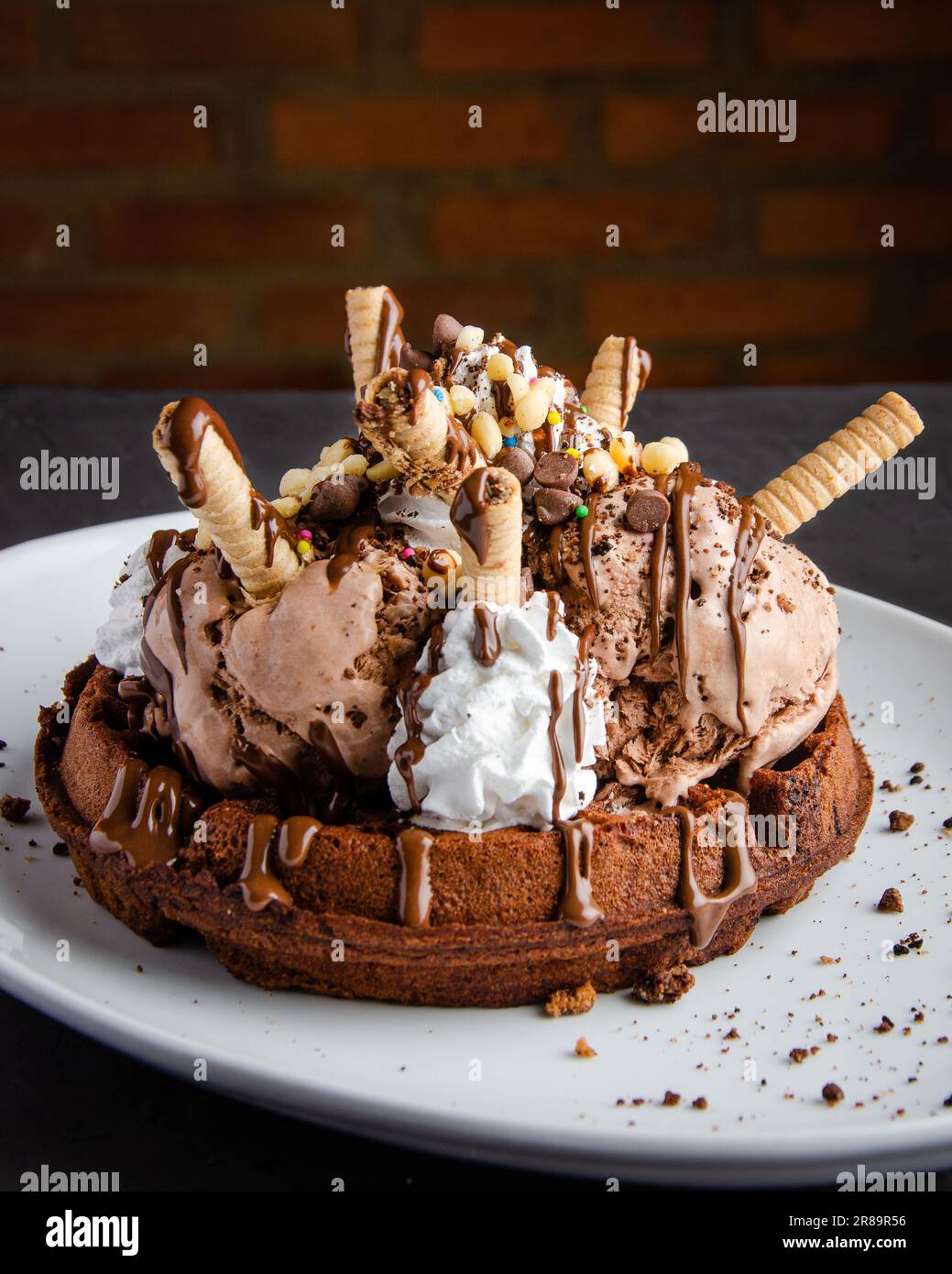 Gelato al cioccolato e waffle, con crema e sciroppo di cioccolato, fondo nero, muro di mattoni Foto Stock