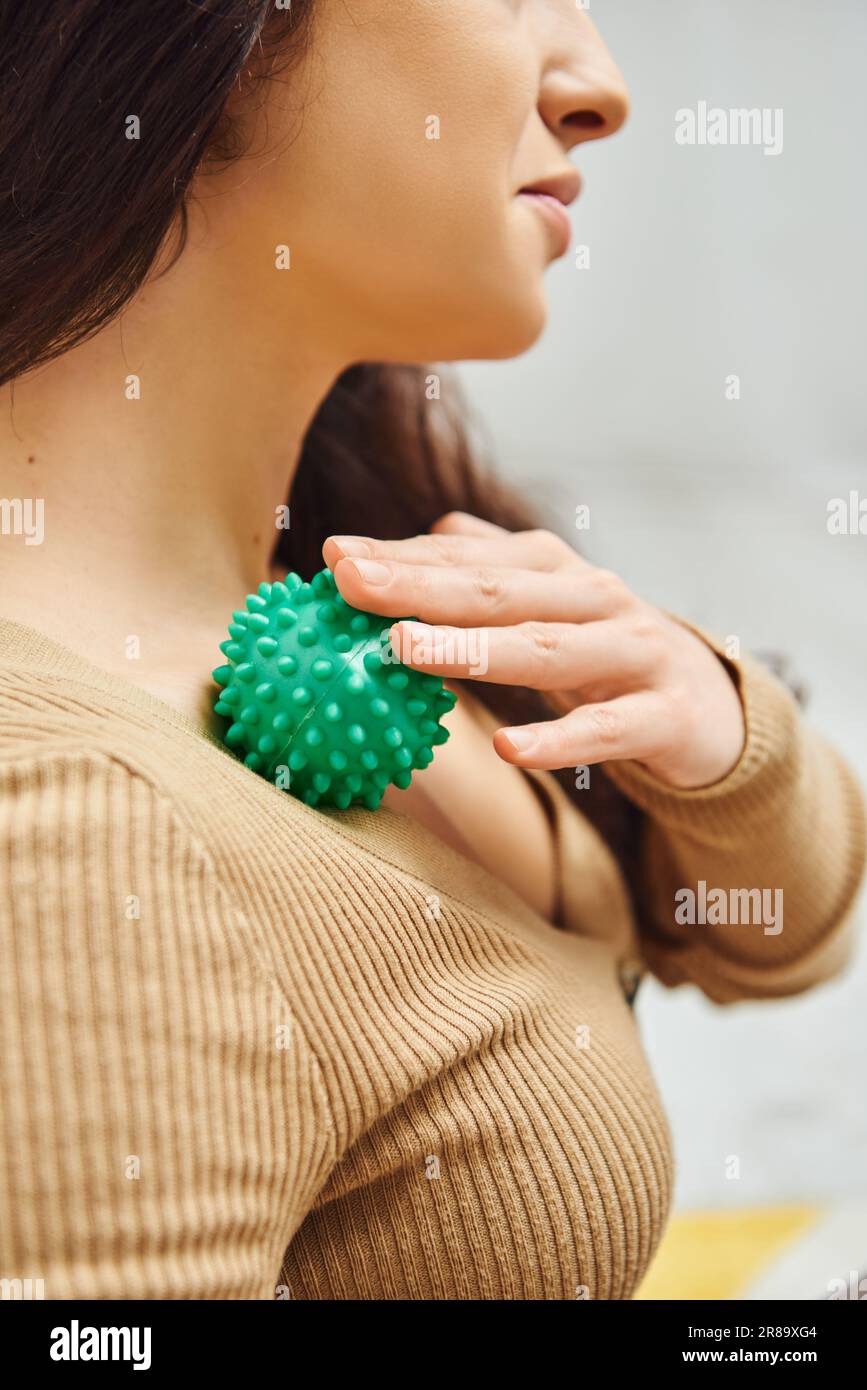 Vista ritagliata della donna brunetta in jumper marrone sistema linfatico massaggiante sul petto con pallina massaggio manuale a casa, rituale self-care e olistico wel Foto Stock