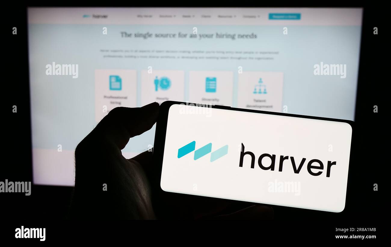 Persona che possiede il cellulare con il logo della società di gestione dei talenti Harver B.V. sullo schermo davanti alla pagina Web. Concentrarsi sul display del telefono. Foto Stock