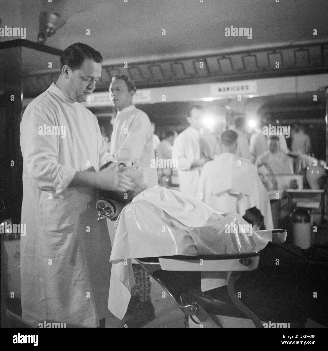 Corrente 22-1-1947: Il passato in un'ora di visitoPer un'ora ogni mattina, l'elettricità viene spenta a Oslo, come tanti altri luoghi del paese. A Oslo, il tempo di disconnessione è 11,30–12,30, in altri luoghi ci possono essere altri tempi. – L'interruzione dell'alimentazione provoca una significativa interruzione del lavoro per le aziende che dipendono dall'elettricità per le loro macchine. Cecil Barbersalong si trova su un piano seminterrato, ma la luce viene risparmiata grazie a numerose potenti lampade a cherosene. Tuttavia, i rasaerba elettrici devono essere azionati manualmente tra 11,30 e 12,30. Foto: TH. Skotaam / Aktuell / NTB Foto Stock