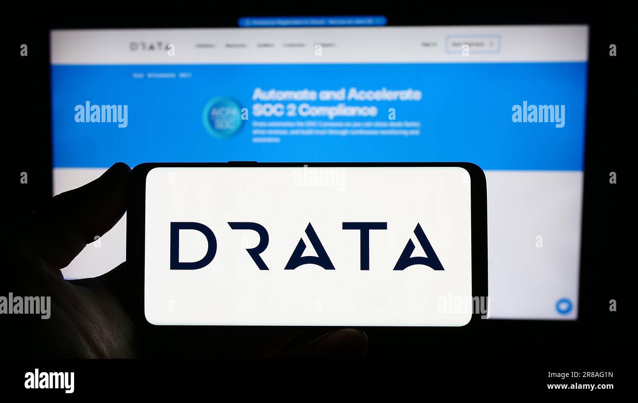 Persona che possiede uno smartphone con il logo della società di soluzioni per la conformità statunitense Drata Inc. Sullo schermo di fronte al sito Web. Concentrarsi sul display del telefono. Foto Stock