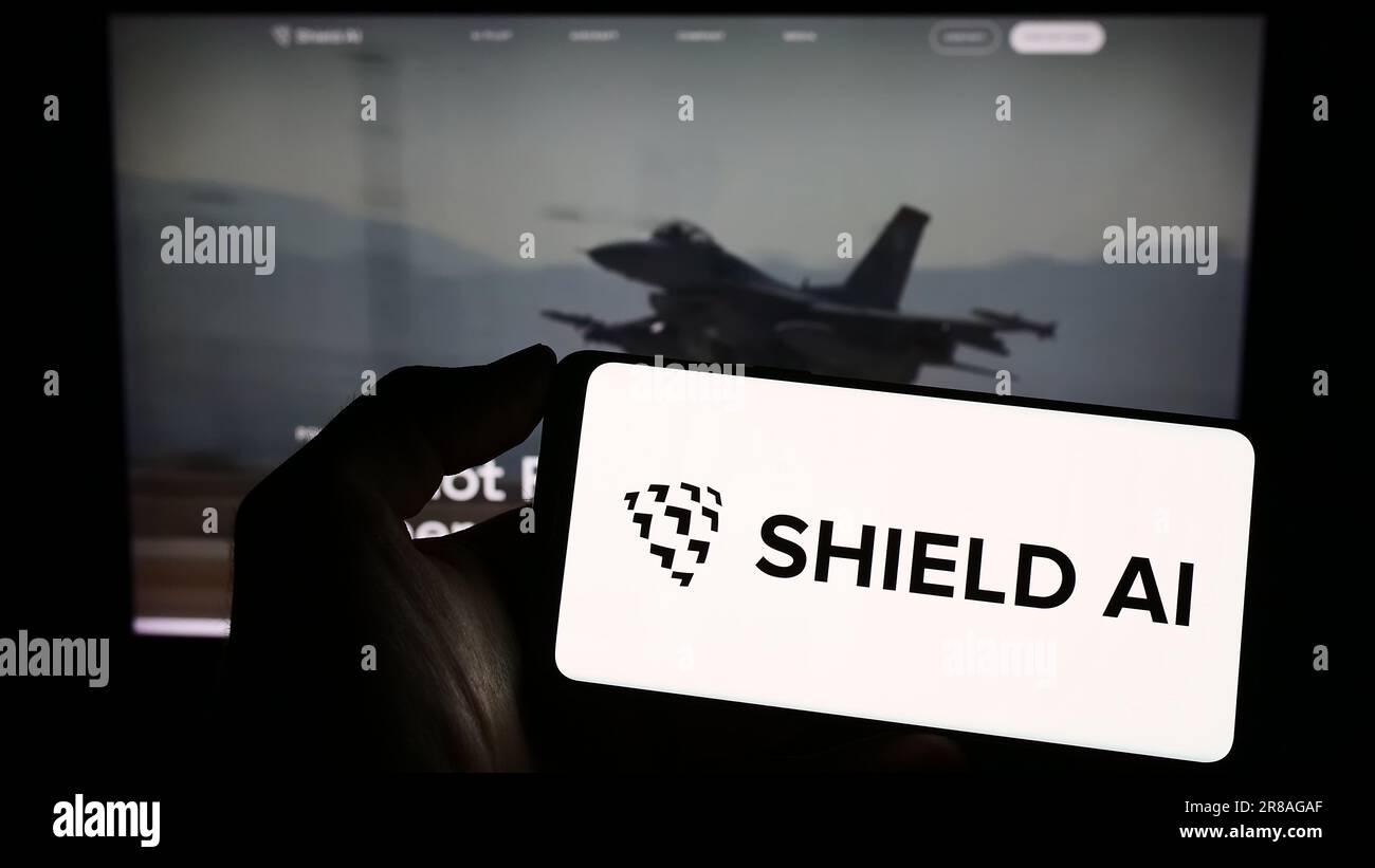 Persona in possesso di un cellulare con il logo della società statunitense per il settore aerospaziale e della difesa Shield ai sullo schermo davanti alla pagina Web aziendale. Concentrarsi sul display del telefono. Foto Stock